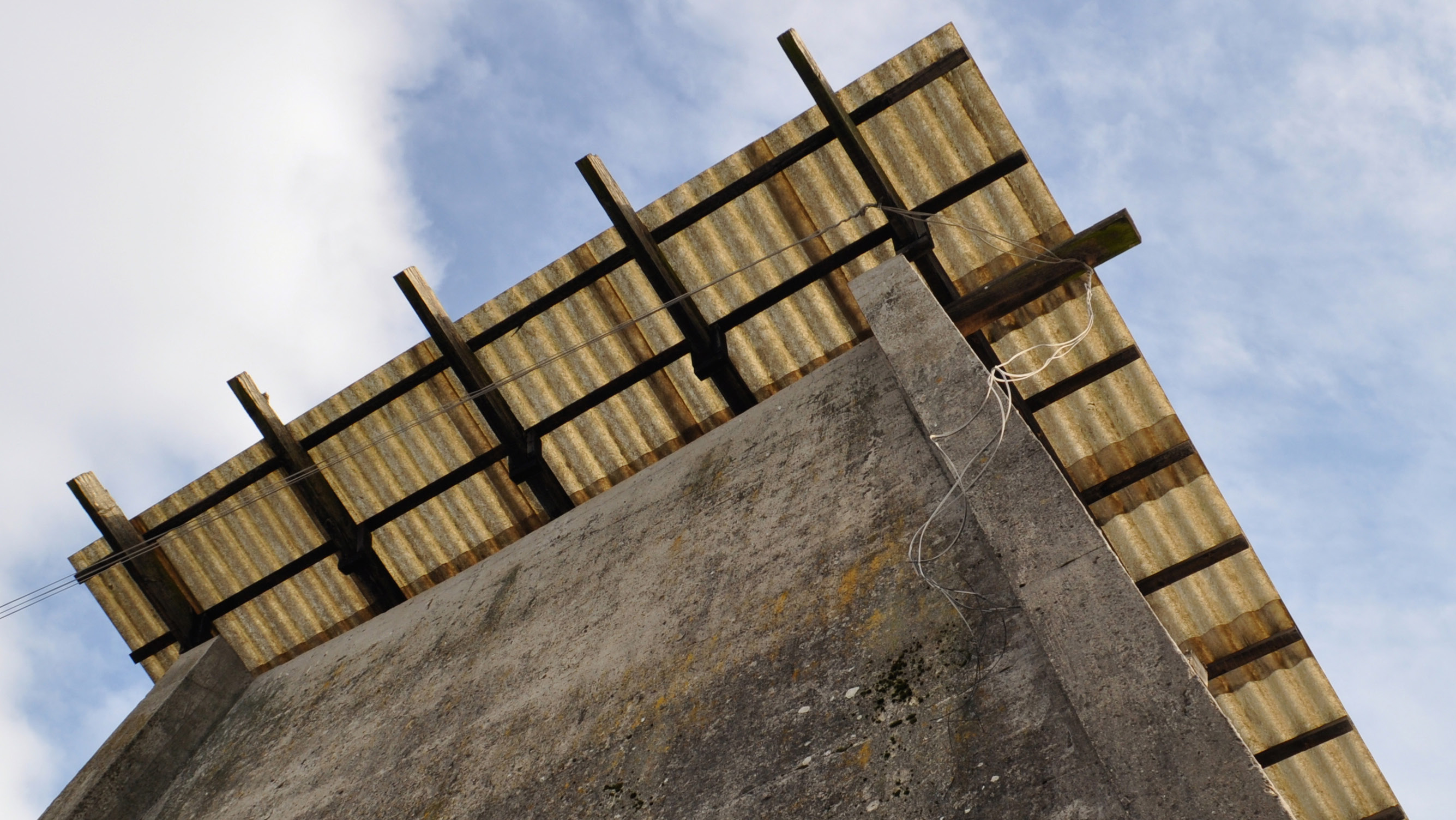 Man sieht ein Betongebäude mit einem Dach aus Wellpappe aus der Froschperspektive