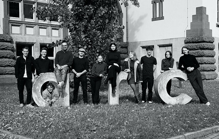 Gruppenfoto der Fachschaft der Fachrichtung Architektur für den Zeitraum 2024/25 am, in beton gegossenem, ARC-Schriftzug vor dem Gebäude Schlüterstraße